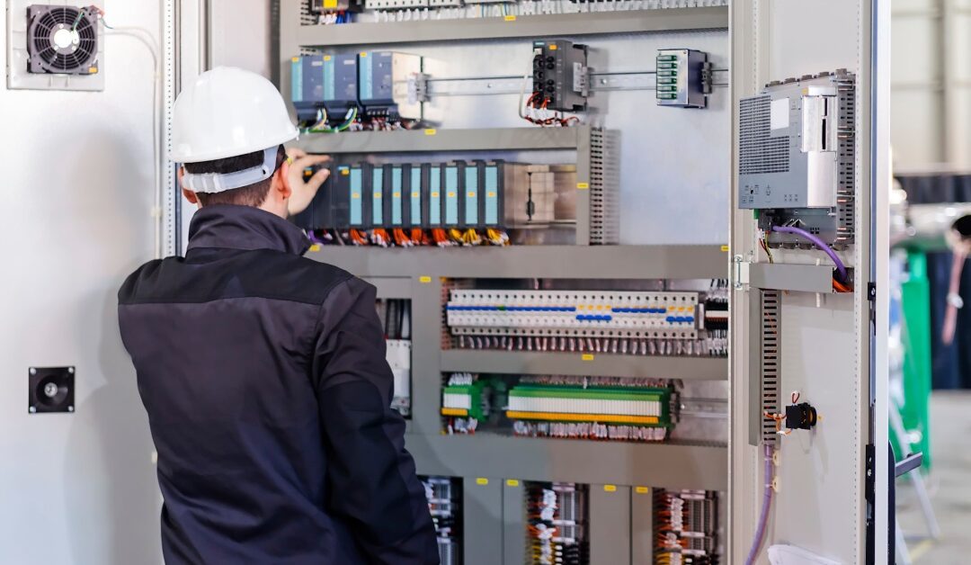 An industrial worker wearing a hard hat opens up an industrial control panel to perform some maintenance checks.