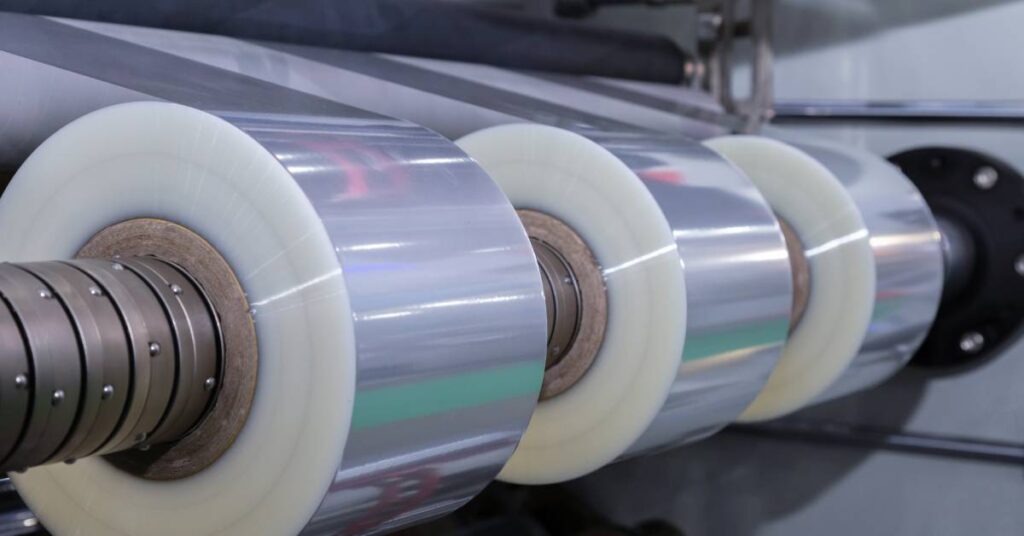 A roll of plastic packaging film sitting atop an automatic packing machine in a food product factory.